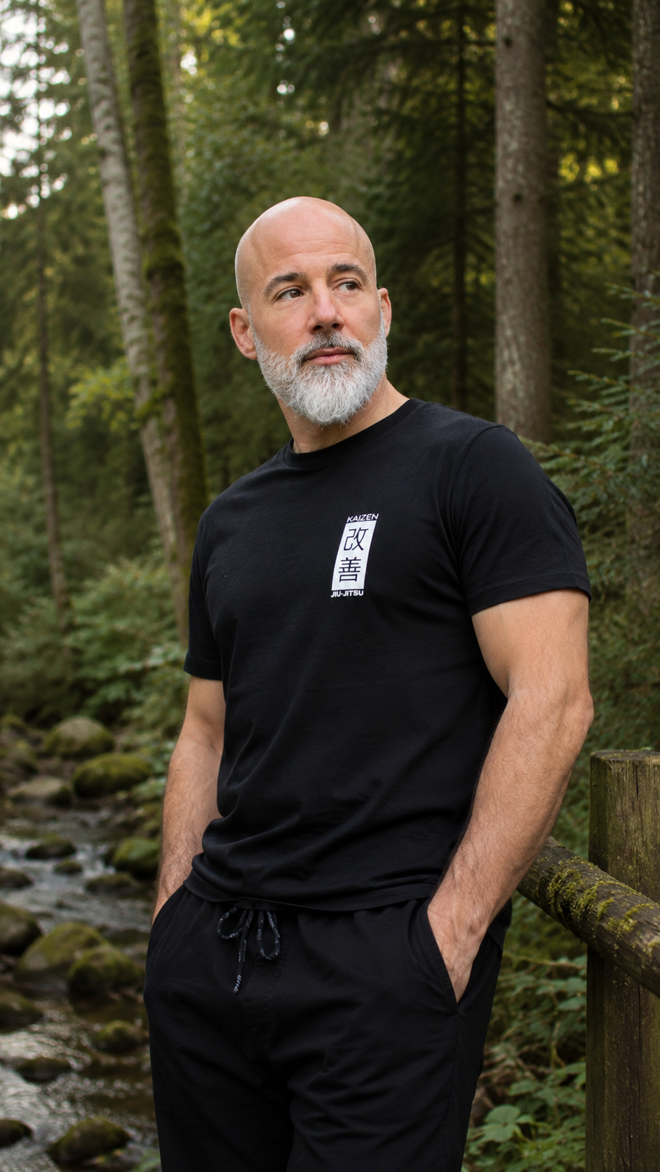 Mann im schwarzen Kaizen Jiu-Jitsu T-Shirt im Wald – Bio-Baumwolle, mossgrünes Brustlogo, Frontansicht