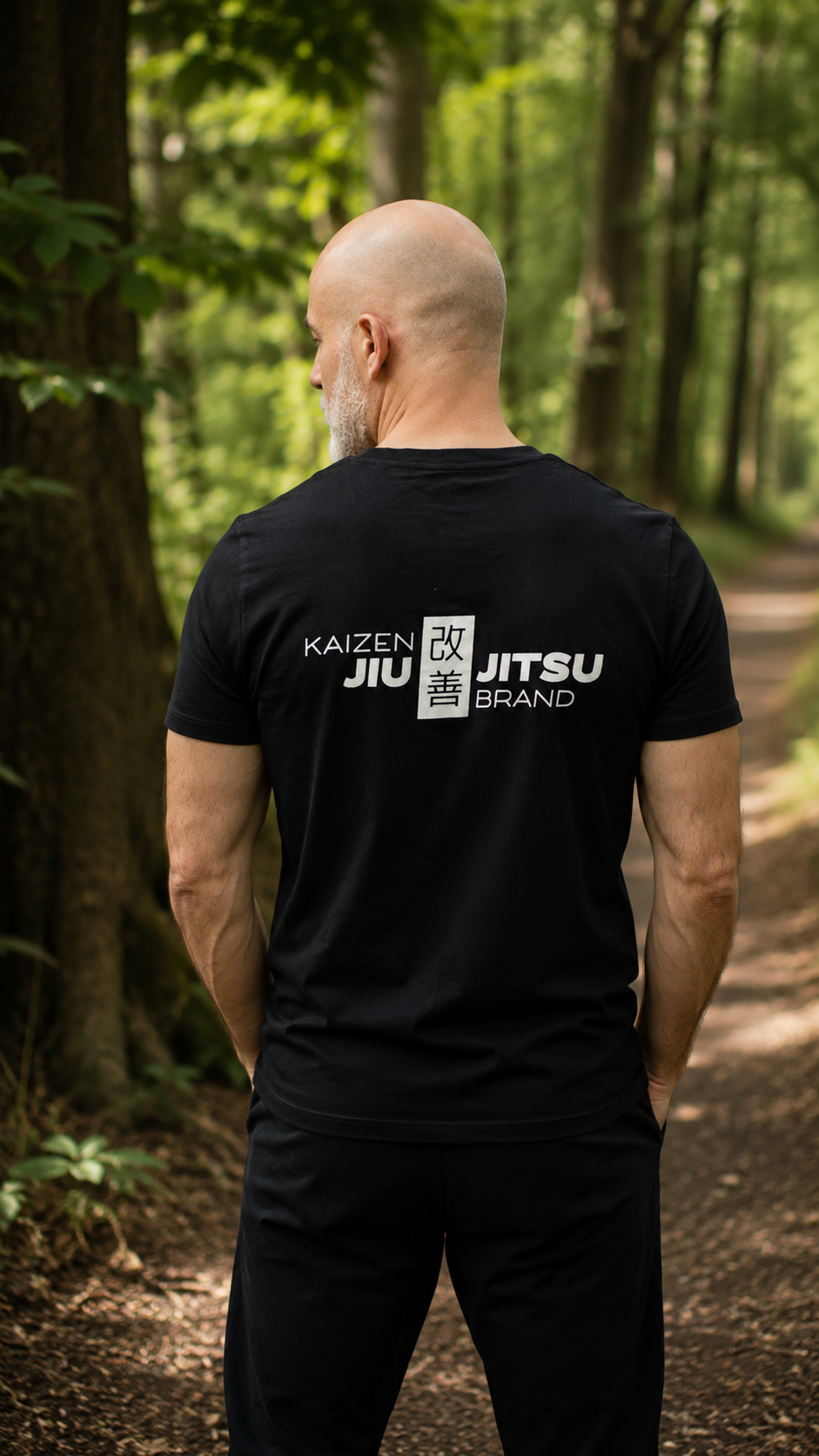 Mann im schwarzen Kaizen Jiu-Jitsu T-Shirt von hinten – grosses Rückenlogo, Waldweg, Rückansicht