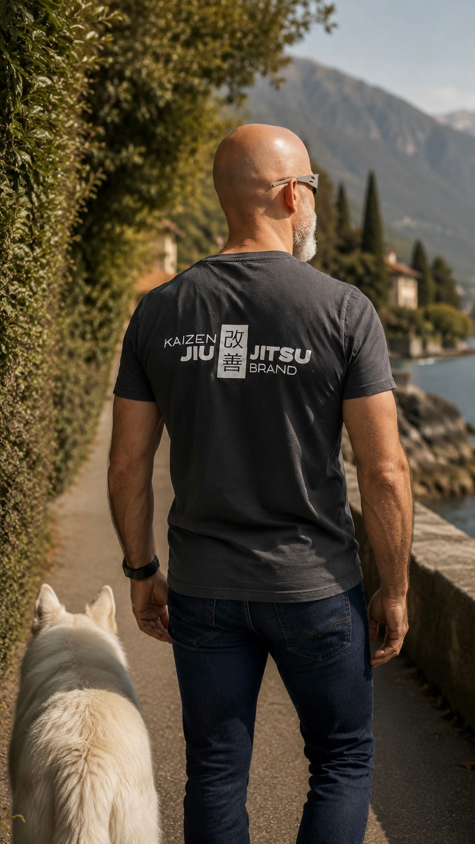 Mann im grauen Kaizen T-Shirt mit Hund an der Seepromenade – Rückansicht