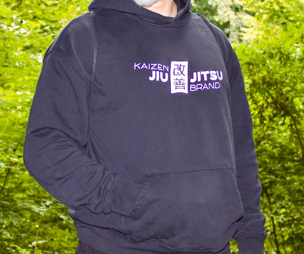 Mann im dunklen Kaizen Black Label Hoodie mit Kängurutasche im Grünen – BJJ Streetwear, Frontansicht